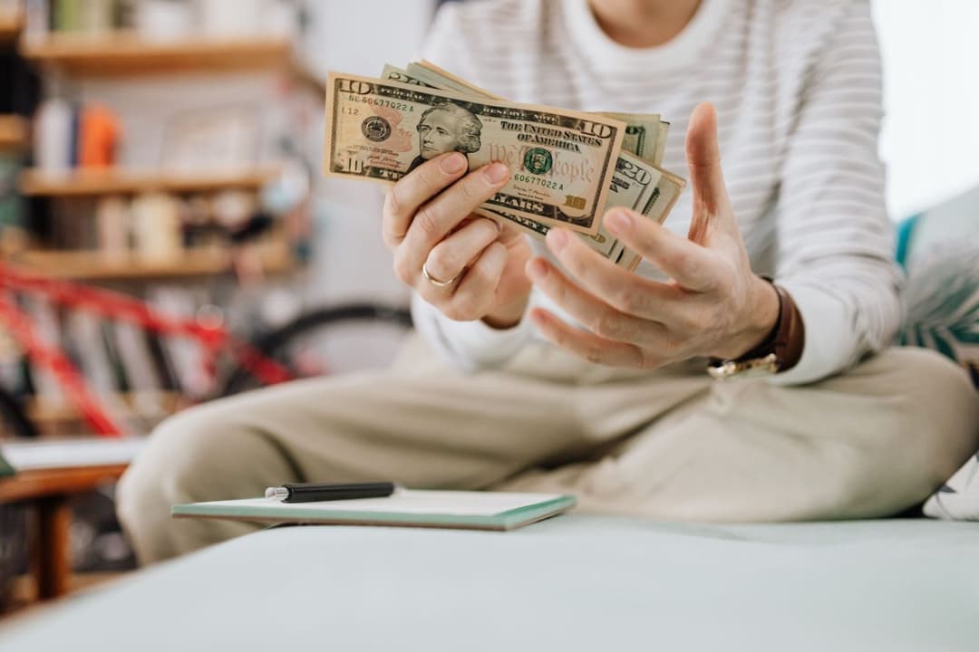 Person holding a fan of U.S. dollar bills over a notebook and pen